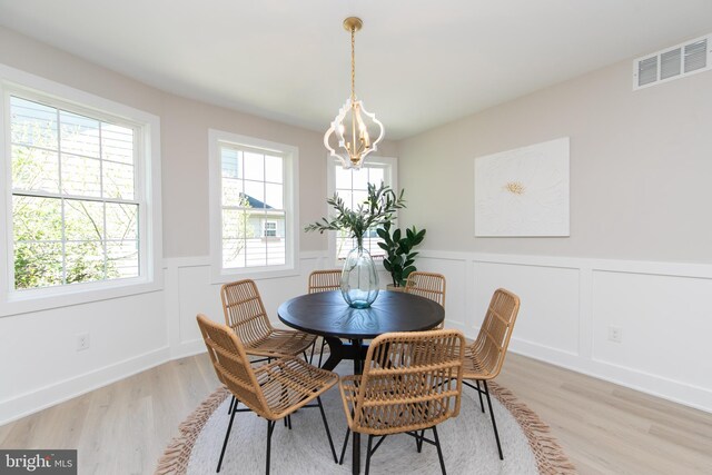 dining area featuring a decorative wall, wainscoting, light wood-style floors, visible vents, and a notable chandelier