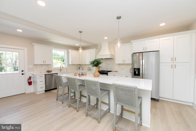 kitchen with white cabinetry, stainless steel appliances, light countertops, premium range hood, and light wood-type flooring