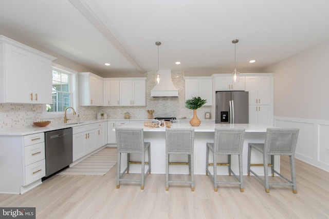 kitchen with white cabinetry, a sink, light wood-style floors, stainless steel appliances, and custom exhaust hood