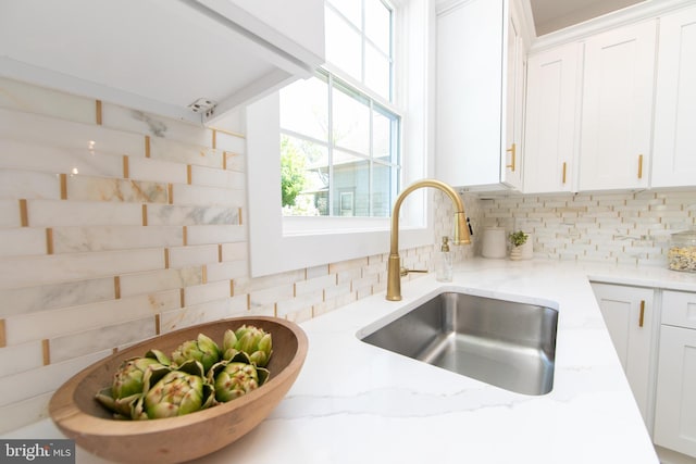 room details with light stone countertops, backsplash, white cabinets, and a sink