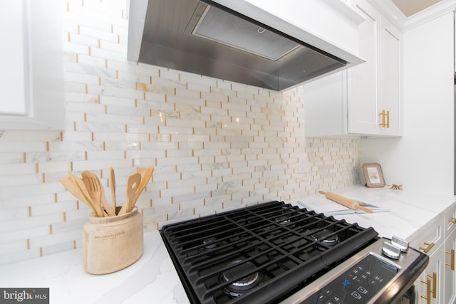 kitchen with tasteful backsplash, light stone countertops, gas range, white cabinetry, and wall chimney exhaust hood