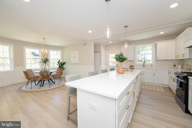 kitchen featuring light wood-style floors, black electric range oven, visible vents, a kitchen island, and wainscoting