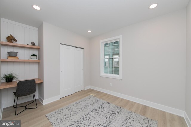 bedroom featuring light wood-style floors, a closet, built in desk, and baseboards