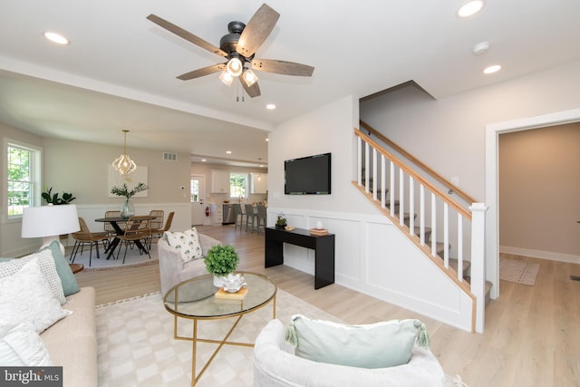 living area featuring a wealth of natural light, visible vents, light wood-style flooring, and wainscoting