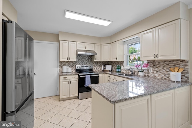 kitchen with a peninsula, freestanding refrigerator, under cabinet range hood, a sink, and stainless steel range with electric stovetop
