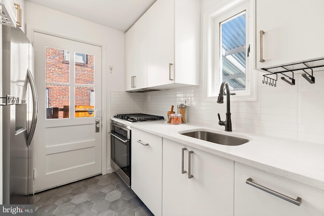 kitchen with appliances with stainless steel finishes, a sink, tile patterned floors, white cabinetry, and backsplash