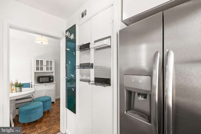 kitchen with stainless steel refrigerator with ice dispenser, white cabinets, black microwave, and visible vents