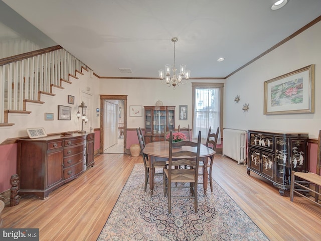 dining room with an inviting chandelier, ornamental molding, radiator, and light wood-style floors