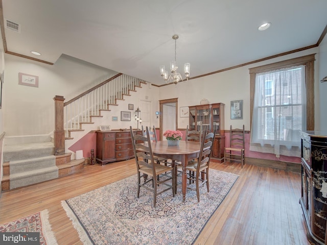 dining room with an inviting chandelier, hardwood / wood-style floors, stairs, visible vents, and ornamental molding