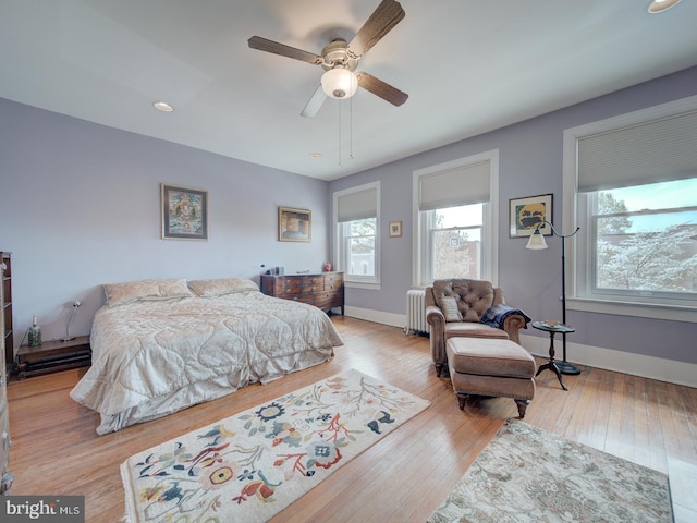 bedroom with a ceiling fan, baseboards, radiator, and hardwood / wood-style floors
