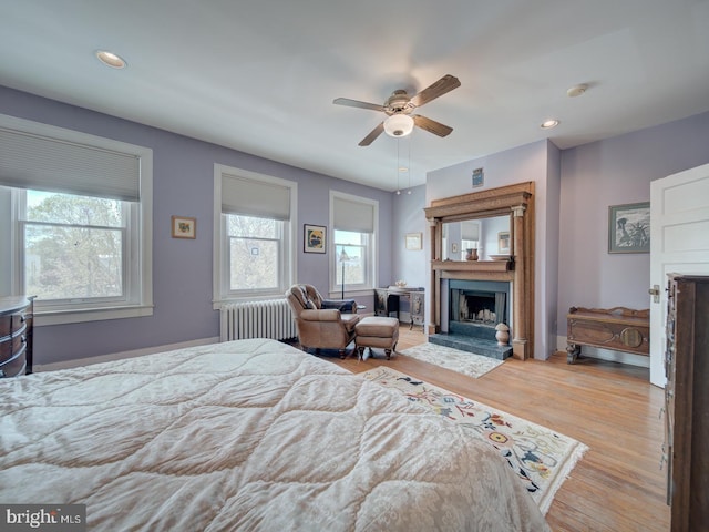 bedroom with radiator, multiple windows, a fireplace with raised hearth, and wood finished floors