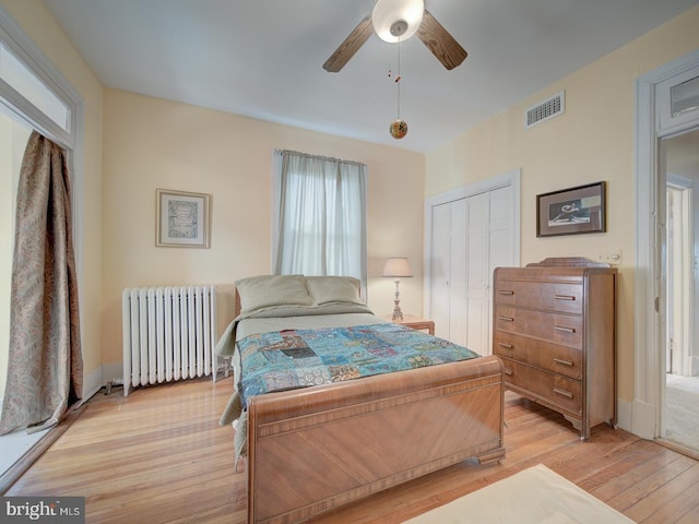 bedroom featuring ceiling fan, visible vents, a closet, light wood finished floors, and radiator heating unit
