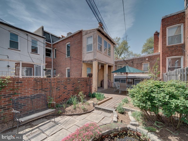 rear view of house with outdoor dining area, brick siding, fence, and a deck