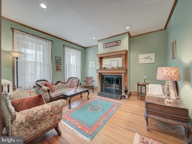 living area featuring ornamental molding, a fireplace with raised hearth, recessed lighting, and wood finished floors
