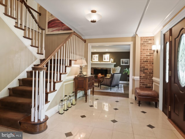 tiled entrance foyer with stairway, a brick fireplace, and crown molding