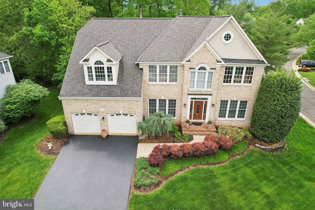 colonial inspired home with an attached garage, brick siding, driveway, a front lawn, and a shingled roof