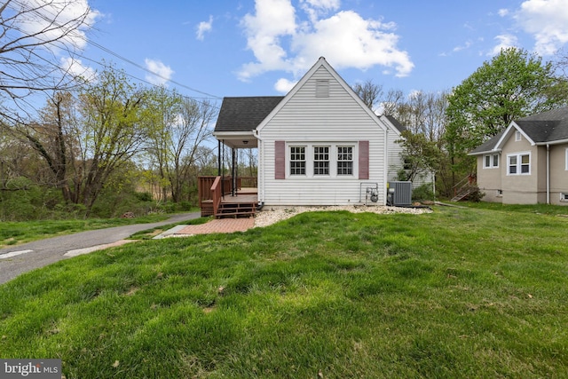 back of house with cooling unit, a lawn, a wooden deck, and roof with shingles