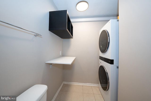 laundry area with baseboards, stacked washing maching and dryer, and light tile patterned floors