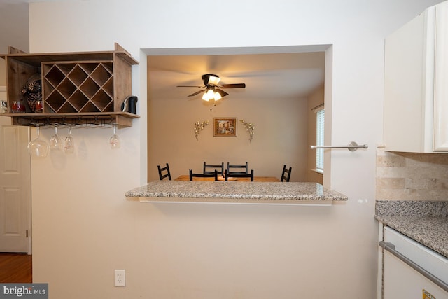 kitchen with light stone counters, a ceiling fan, white cabinetry, wood finished floors, and backsplash
