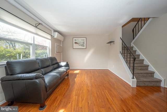 living area with baseboards, an AC wall unit, stairs, and wood finished floors