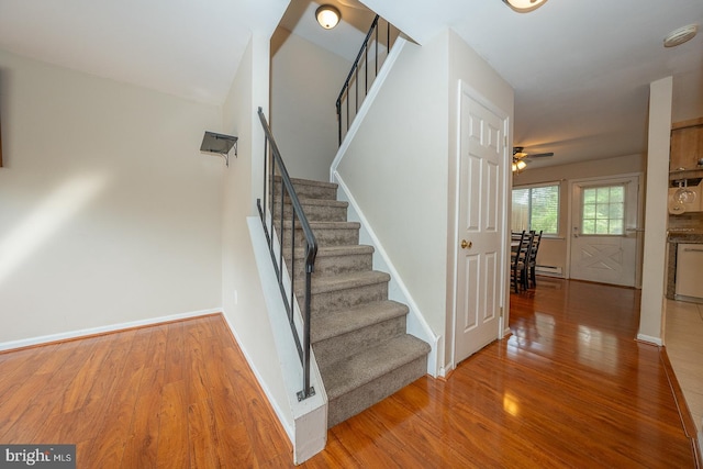 staircase featuring baseboards, baseboard heating, ceiling fan, and wood finished floors