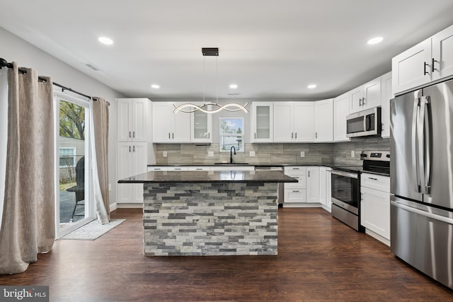 kitchen with dark stone countertops, a sink, decorative backsplash, glass insert cabinets, and appliances with stainless steel finishes