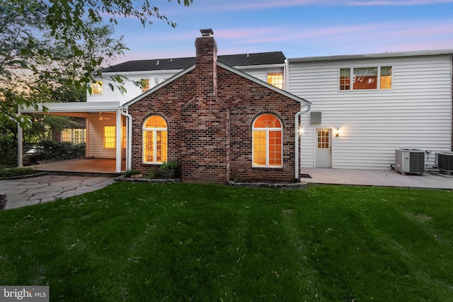 13148 Isle Of Mann Way, Highland, MD 20777 - back of property at dusk with a patio, cooling unit, a lawn, a chimney, and brick siding