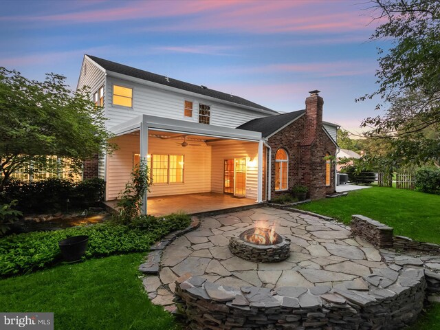 13148 Isle Of Mann Way, Highland, MD 20777 - back of property at dusk with an outdoor fire pit, a patio area, a lawn, and a chimney