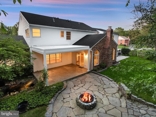13148 Isle Of Mann Way, Highland, MD 20777 - back of property at dusk featuring a patio, an outdoor fire pit, a shingled roof, and a chimney