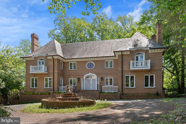 colonial house with fence, a chimney, brick siding, and a balcony