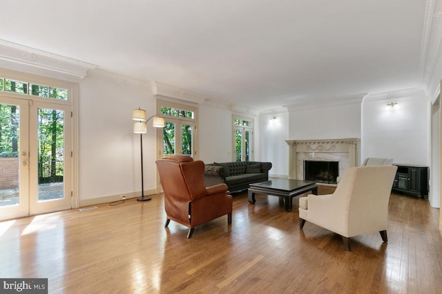 living area with crown molding, a fireplace, french doors, light wood-style flooring, and baseboards