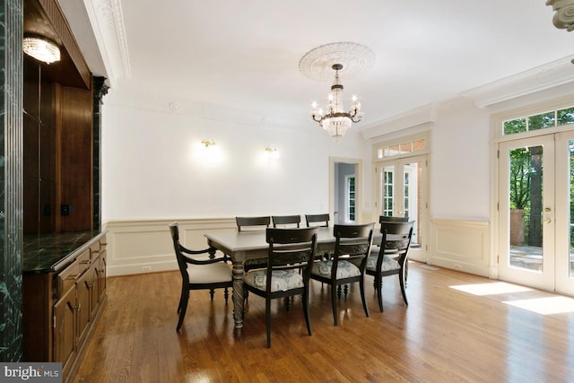 dining space with a decorative wall, a chandelier, french doors, wood finished floors, and ornamental molding