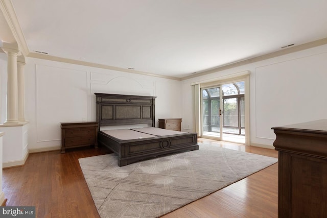 bedroom featuring ornamental molding, decorative columns, wood finished floors, and access to exterior