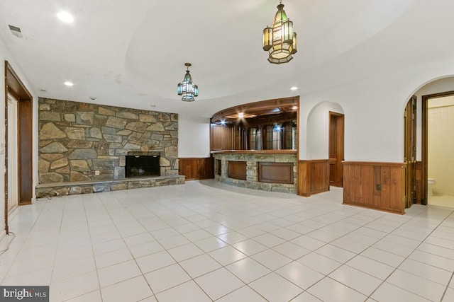 unfurnished living room with a fireplace, arched walkways, visible vents, and a wainscoted wall