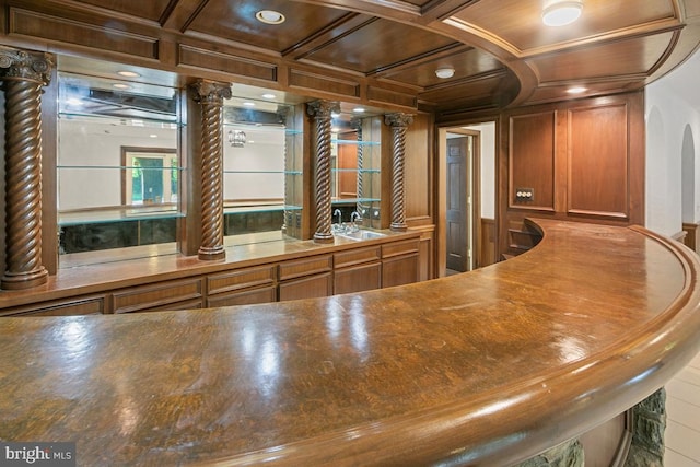 bar featuring a sink, arched walkways, coffered ceiling, and wet bar