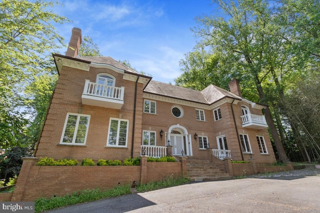 view of front of home featuring brick siding, a balcony, and a chimney