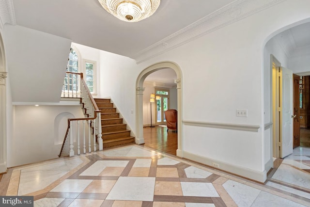 foyer featuring stairs, arched walkways, baseboards, and ornamental molding