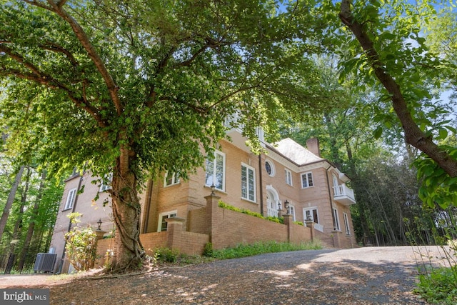 view of property exterior featuring central air condition unit, a chimney, and brick siding