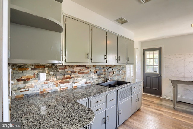kitchen featuring backsplash, a sink, light wood-style floors, dark stone counters, and gray cabinetry