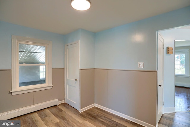 empty room with baseboard heating, a wainscoted wall, and wood finished floors