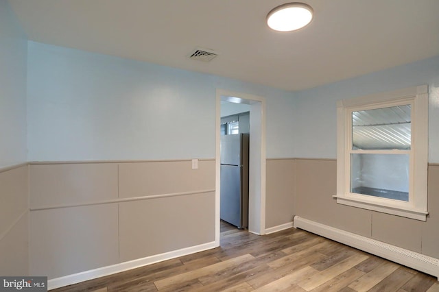 spare room featuring baseboard heating, baseboards, wood finished floors, and visible vents