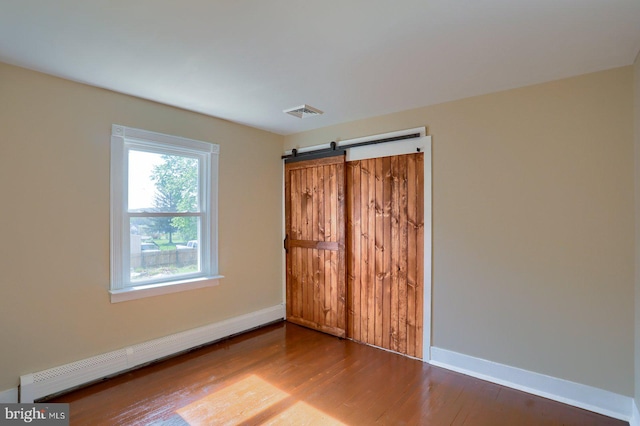 empty room featuring baseboards, wood finished floors, a baseboard radiator, and a barn door