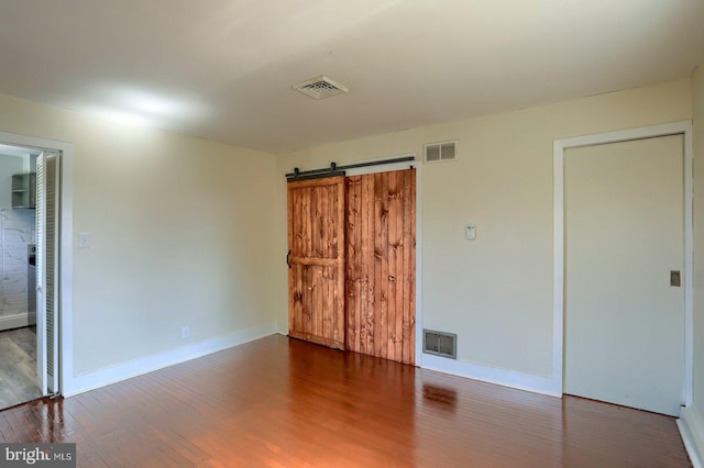 unfurnished bedroom with a barn door, wood finished floors, and visible vents