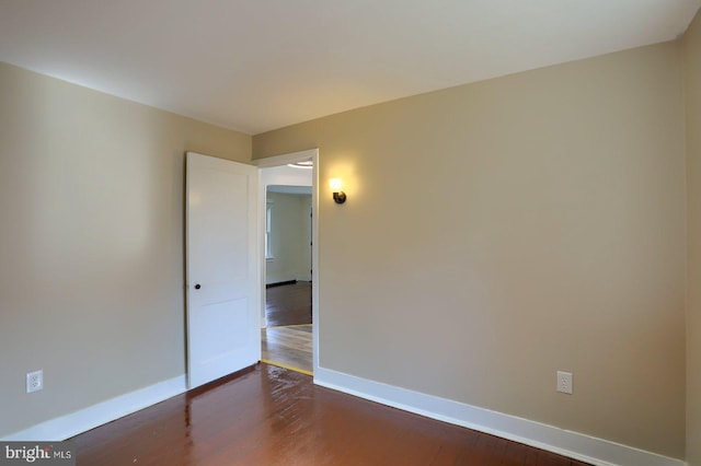 spare room featuring dark wood-type flooring and baseboards