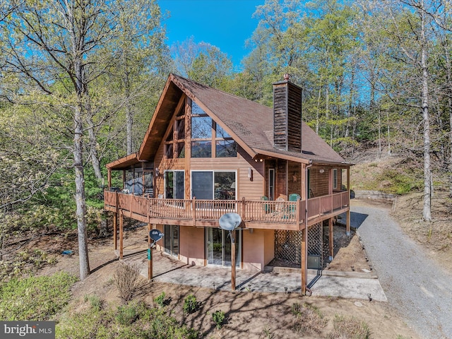 back of property featuring a patio, a wooden deck, roof with shingles, and a chimney