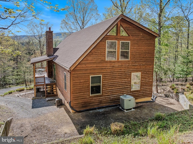 view of side of property with a shingled roof, central AC unit, a chimney, and a wooden deck