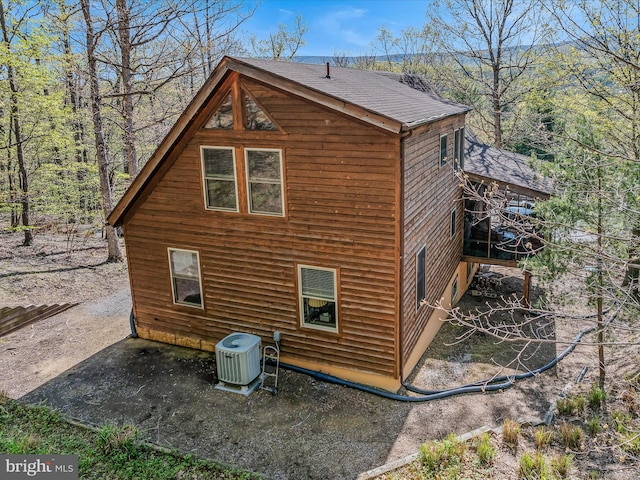 view of side of property with central AC unit and a shingled roof