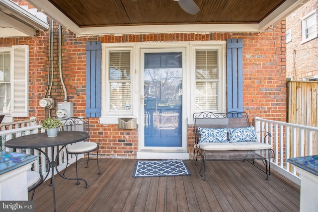 doorway to property featuring a ceiling fan, a porch, and brick siding