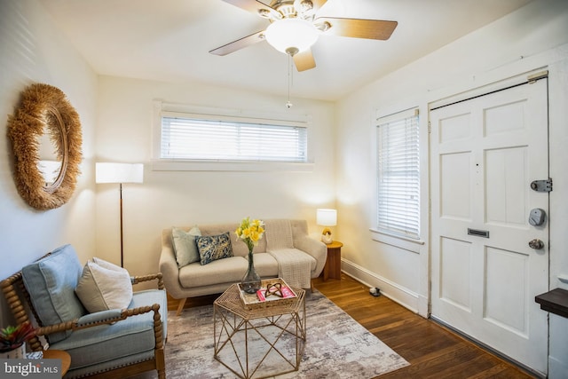 living area featuring baseboards, a ceiling fan, and dark wood-type flooring