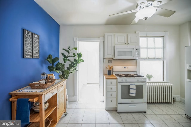 kitchen featuring a ceiling fan, baseboards, radiator, white appliances, and white cabinetry